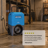 A blue and gray Dri-Eaz LGR 7000XLi commercial dehumidifier standing on a concrete warehouse floor next to a wall, with shelving in the background and a large customer 5 star review card overlaid in the lower right corner. "I keep buying more of these"