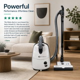 A white and black SEBO Airbelt E3 upright vacuum cleaner shown in a bright, modern living room setting next to a beige sofa and wooden floor. The image includes promotional text and 5 star review on the left side.