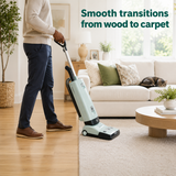 Person using a mint vacuum cleaner on a wooden floor in a living room.